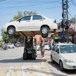 A forklift operator transports illegally parked car elevated above the road at a busy city intersection