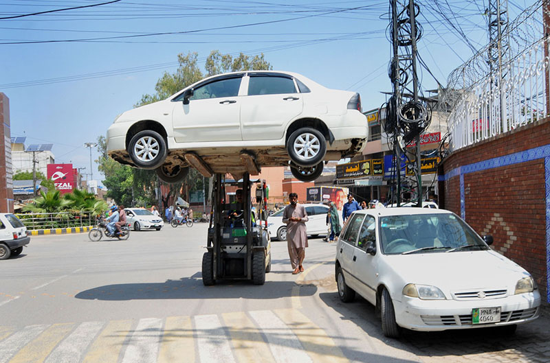 A forklift operator transports illegally parked car elevated above the road at a busy city intersection