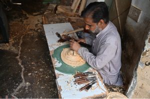 A woodworker guides a slab of raw timber through a surface planer in a local carpentry shop, where raw materials are transformed into finished products for the domestic market