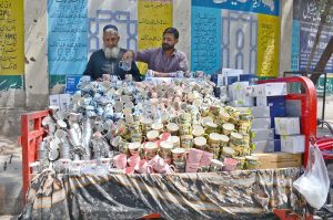 Vendor arranging and displaying different tea cups to attract customers at roadside on tricycle loader.