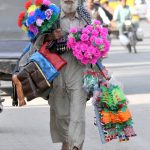 A street hawker carrying colorful artificial flowers and decorative items walks along Vehari Road in search of customers