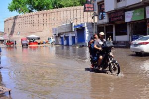 A motorcyclist rides through stagnant rainwater after rainfall while carrying bags of chips on his way in Latifabad