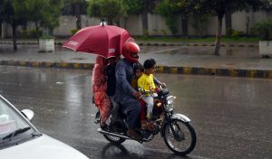 Students ride with their father on a motorcycle, covered with a plastic sheet, while heading to school during heavy rain on the Expressway in the Federal Capital