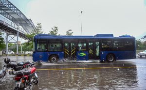 Students ride with their father on a motorcycle, covered with a plastic sheet, while heading to school during heavy rain on the Expressway in the Federal Capital