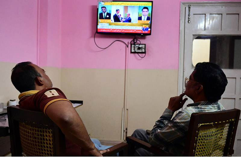 People watch television news coverage of the U.S.–Iran peace talks in Islamabad as diplomatic efforts continue in the capital amid heightened global attention
