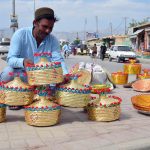 A vendor decorates traditional handwoven Patari baskets with colorful beads and ribbons, highlighting Balochistan’s rich craft heritage and the enduring skill of local artisans