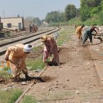 Labourers are busy carrying out maintenance work along a railway track, digging and leveling the ground to ensure safe train operations