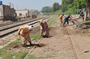 Labourers are busy carrying out maintenance work along a railway track, digging and leveling the ground to ensure safe train operations