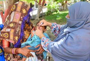A lady health worker administers polio drops to a child as the mother holds the child during the anti-polio campaign.