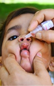 A lady health worker administers polio drops to a child as the mother holds the child during the anti-polio campaign.