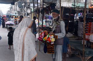 An elderly vendor sells handmade woolen toys to woman