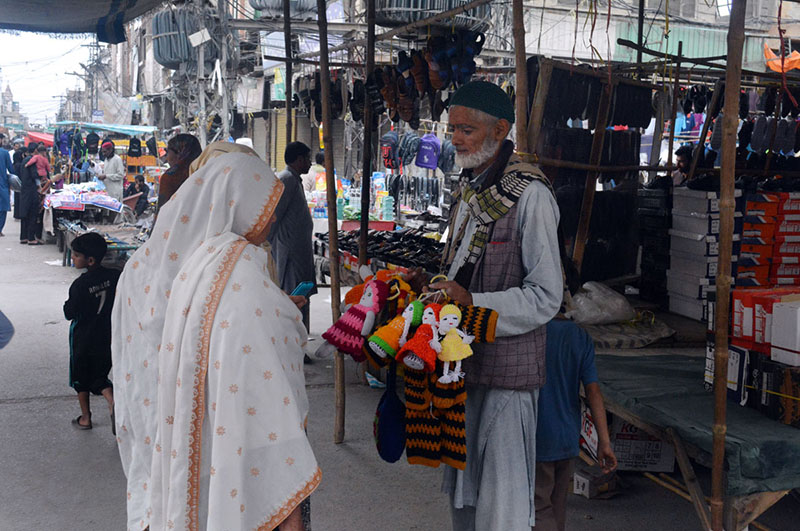 An elderly vendor sells handmade woolen toys to woman