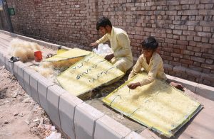 Workers prepare and fill side brackets with straw used in roadside air coolers as demand increases amid rising temperatures.
