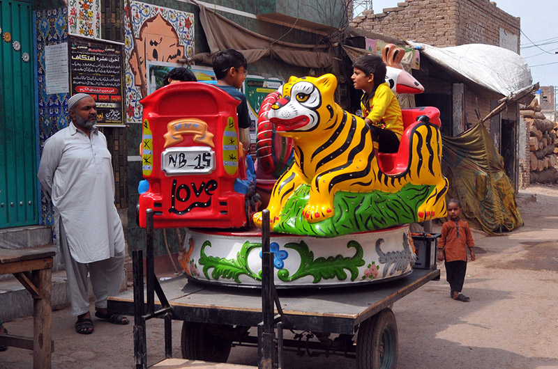 A local street vendor operates a hand-painted, cart-mounted kiddie ride, offering affordable entertainment for children in a bustling neighborhood. These mobile carousels, decorated with vibrant folk art, remain a cherished part of street life