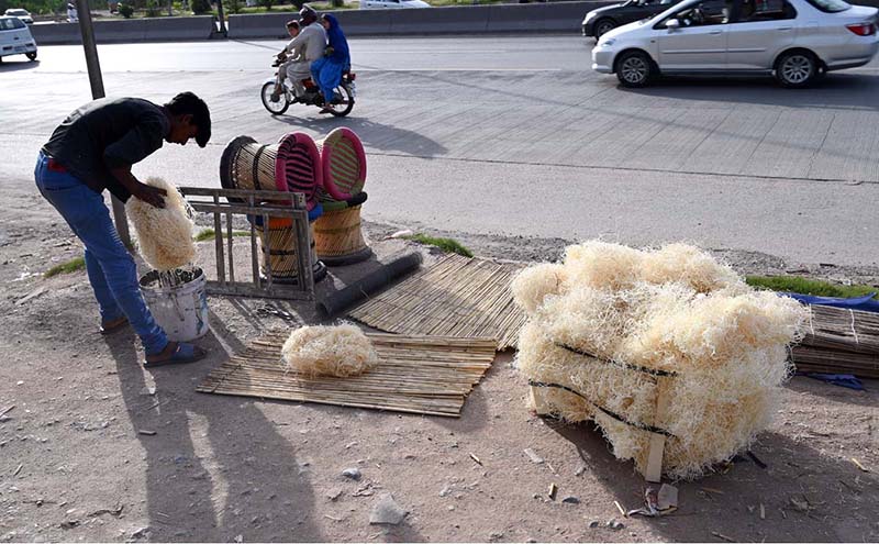 A roadside vendor arranges and prepares husk for room coolers, along with household items and scrubbers for sale beside a busy city road as traffic passes by