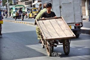 A youngster holding cart while sitting on rear seat of motorcycle at Millat Road