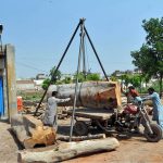 Workers use a simple tripod hoist to lift a large log onto a motorbike trailer at a lumber yard