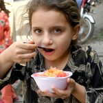 A girl enjoys a bowl of crushed ice from a roadside vendor as temperatures rise in the provincial capital