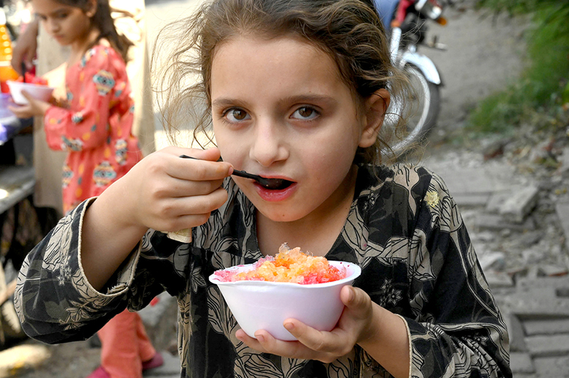 A girl enjoys a bowl of crushed ice from a roadside vendor as temperatures rise in the provincial capital