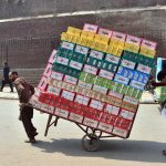Workers push a heavily loaded handcart carrying cardboard boxes used for shoes towards their destination in the city