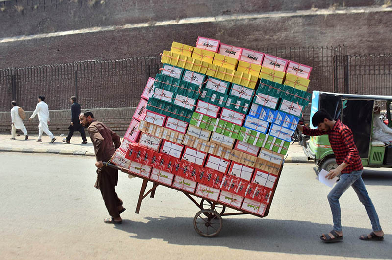 Workers push a heavily loaded handcart carrying cardboard boxes used for shoes towards their destination in the city