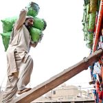 A labourer loading bags filled with vegetable on delivery truck at Vegetable Market