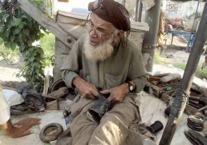 An elderly cobbler busy repairing shoes to earn a livelihood.