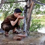 A youngster drinks water from a hand pump to quench his thirst during a hot day in the city