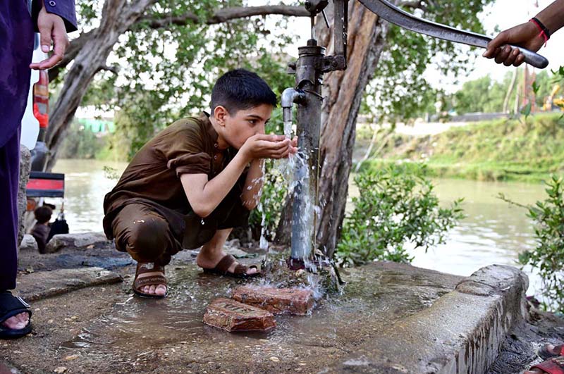 A youngster drinks water from a hand pump to quench his thirst during a hot day in the city
