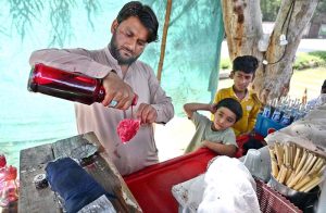 A vendor prepares Ice Gola on his roadside setup for children during a hot day in the city.