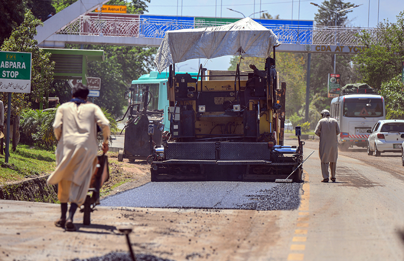 Workers repair a section of Srinagar Highway by laying asphalt during ongoing road maintenance work