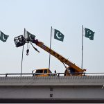 Worker install the Pakistan flag with the help of a crane at fly over in the federal Capital to mark the completion of one year of the victory of Marka-e-Haq Bunyan-ul-Marsoos