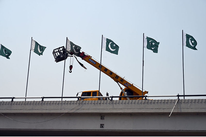 Worker install the Pakistan flag with the help of a crane at fly over in the federal Capital to mark the completion of one year of the victory of Marka-e-Haq Bunyan-ul-Marsoos