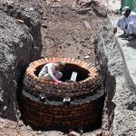 Workers construct a brick manhole inside a trench during ongoing drainage and sewerage development work along a roadside in the city