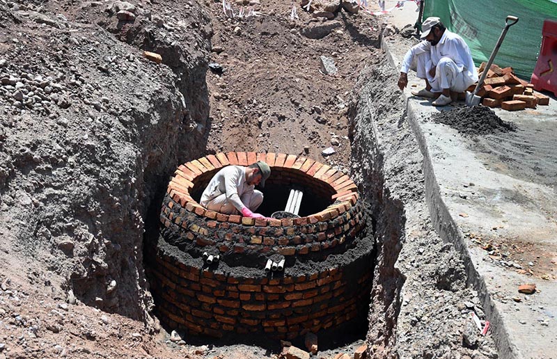 Workers construct a brick manhole inside a trench during ongoing drainage and sewerage development work along a roadside in the city