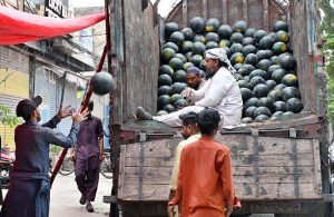 Labourers are busy unloading watermelons from delivery truck at a roadside stall