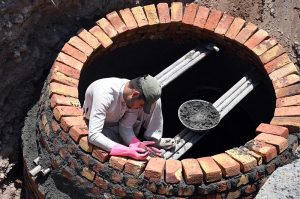 Workers construct a brick manhole inside a trench during ongoing drainage and sewerage development work along a roadside in the city