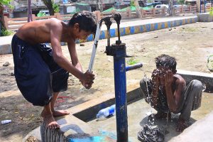 Youngsters cool off under water from a hand pump during hot weather in the city