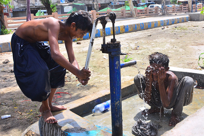 Youngsters cool off under water from a hand pump during hot weather in the city