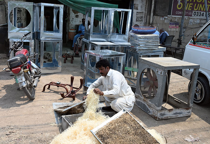 Worker busy in filling husk in frames of room air coolers at his workplace