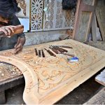 A carpenter is busy carving designs on a wooden piece at his workplace