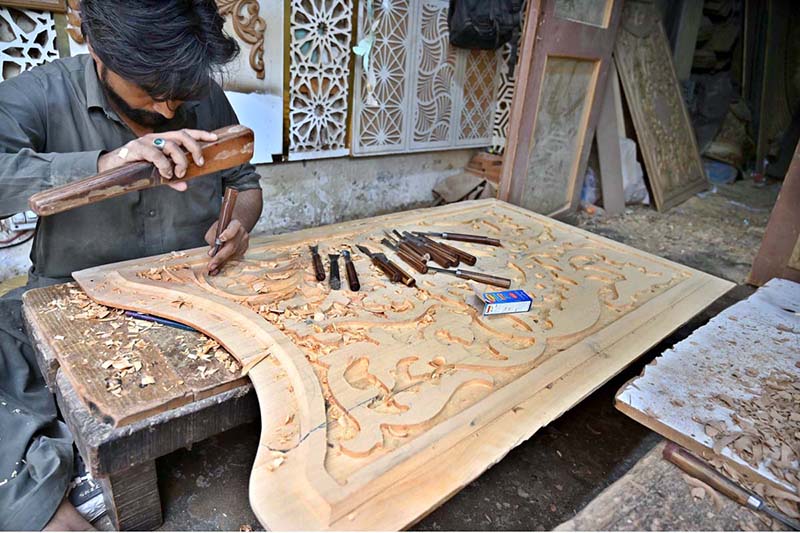 A carpenter is busy carving designs on a wooden piece at his workplace