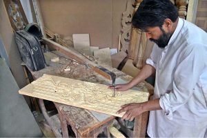 A carpenter is busy carving designs on a wooden piece at his workplace