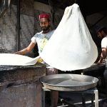 A worker prepares samosa patti on a huge tawa, rolling the dough by hand step by step at his workplace