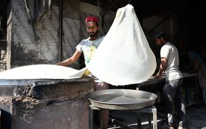 A worker prepares samosa patti on a huge tawa, rolling the dough by hand step by step at his workplace