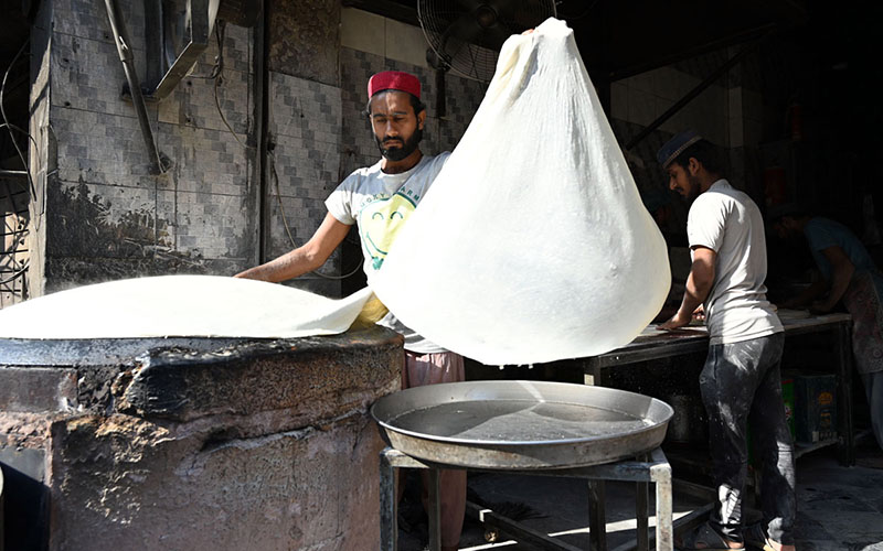 A worker prepares samosa patti on a huge tawa, rolling the dough by hand step by step at his workplace
