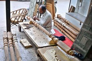 A carpenter is busy carving designs on a wooden piece at his workplace