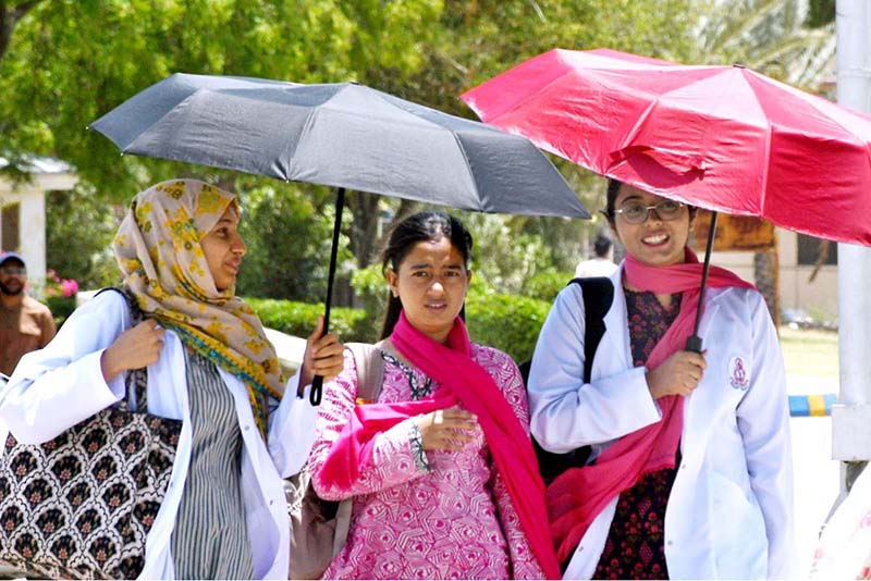 Medical students walk under an umbrella to protect themselves from intense heat and direct sunlight during hot weather at LUMHS Jamshoro