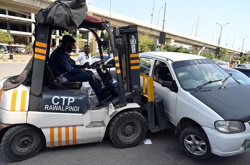 Traffic police personnel remove an illegally parked car with the help of a car lifter along Murree Road in the Commercial Market area