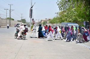 Medical students walk under an umbrella to protect themselves from intense heat and direct sunlight during hot weather at LUMHS Jamshoro